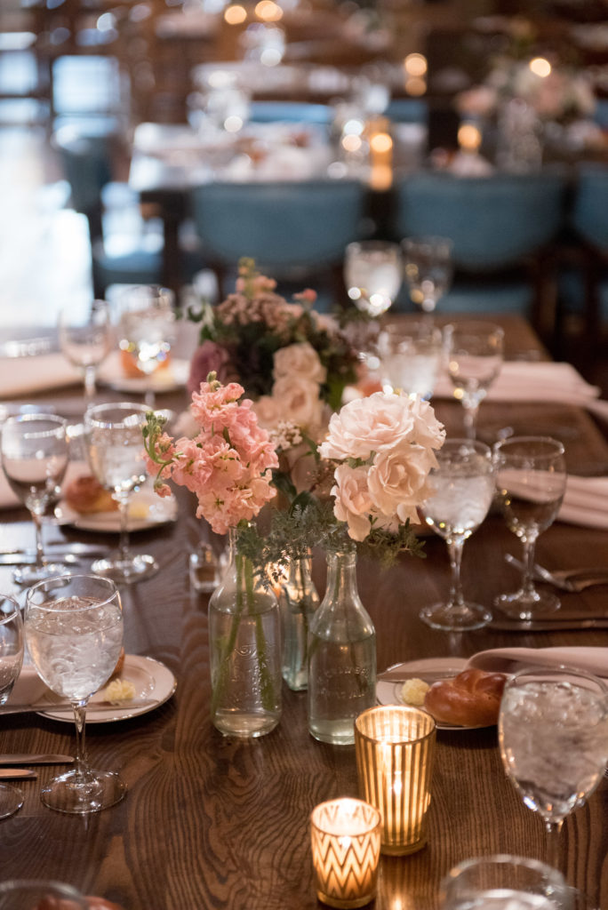 Peach stock and white majolica table centerpieces in vintage bottles for winter wedding at Salvage One.