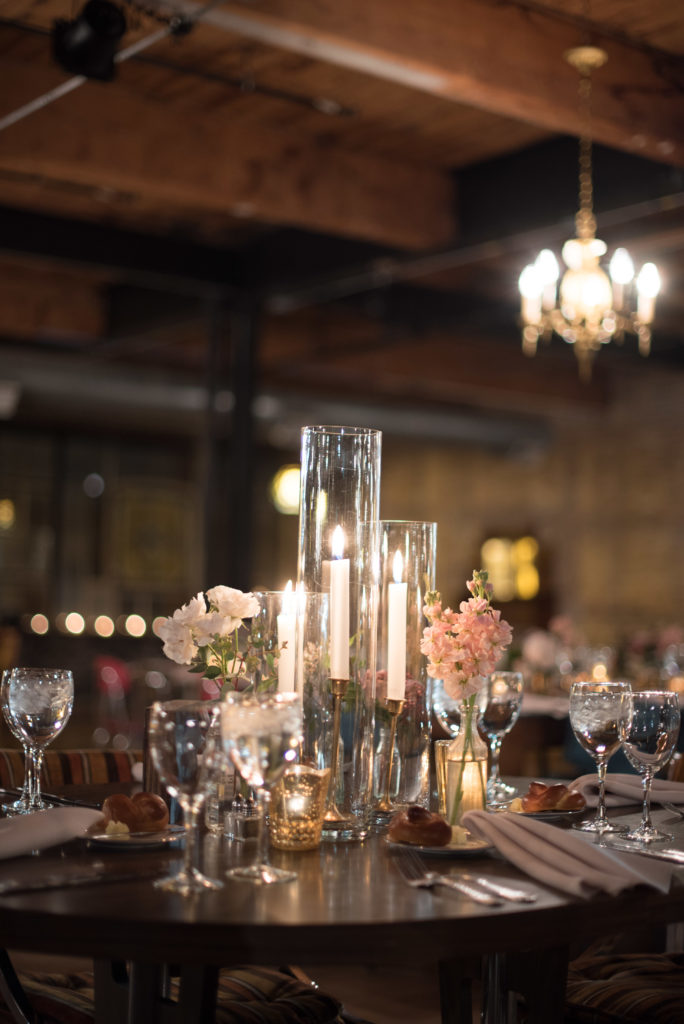 Centerpiece of taper candles with peach stock and spray rose arrangements in vintage glass bottles for winter wedding at Salvage One.