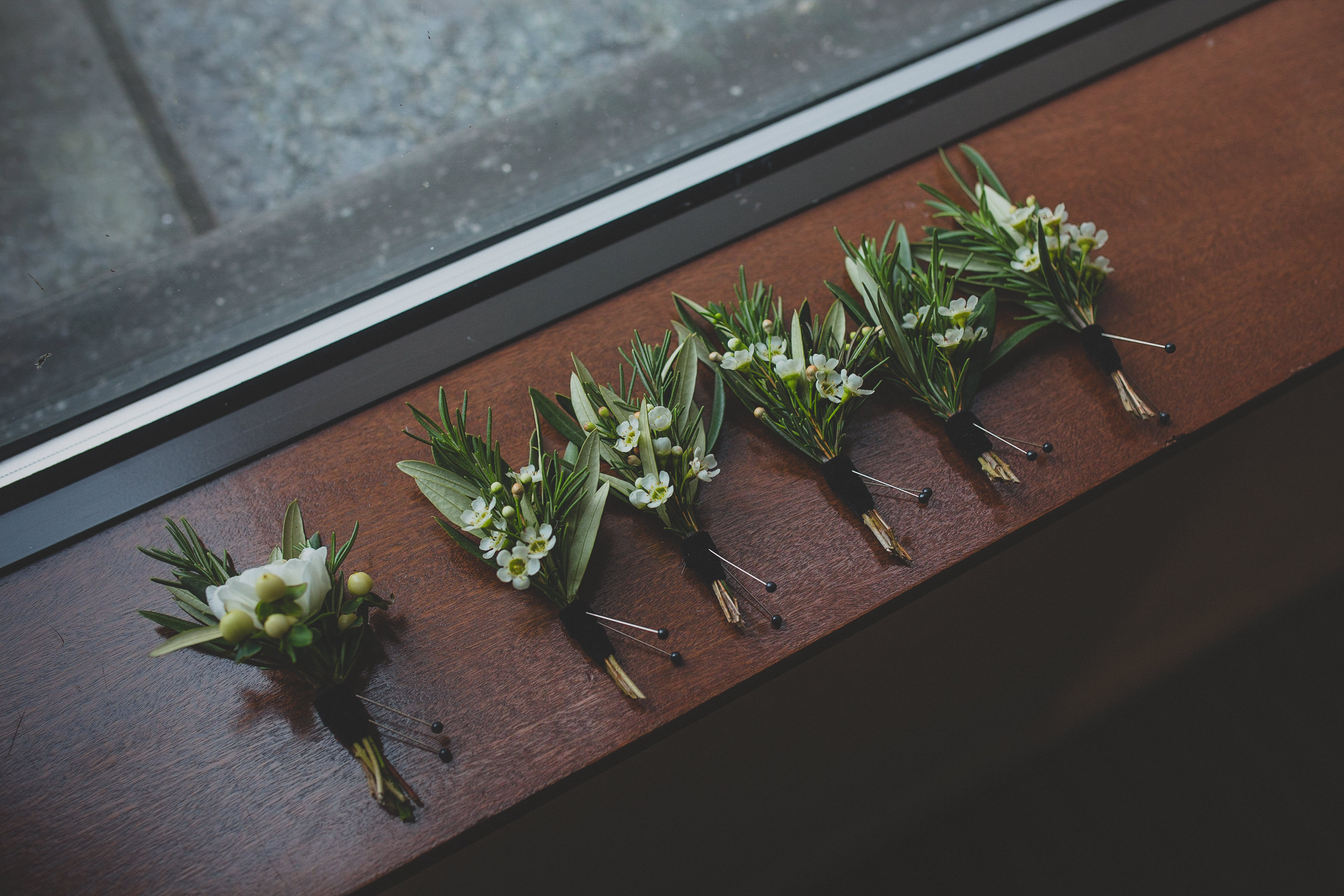 Winter wedding boutonnieres with rosemary, olive, and wax flower.