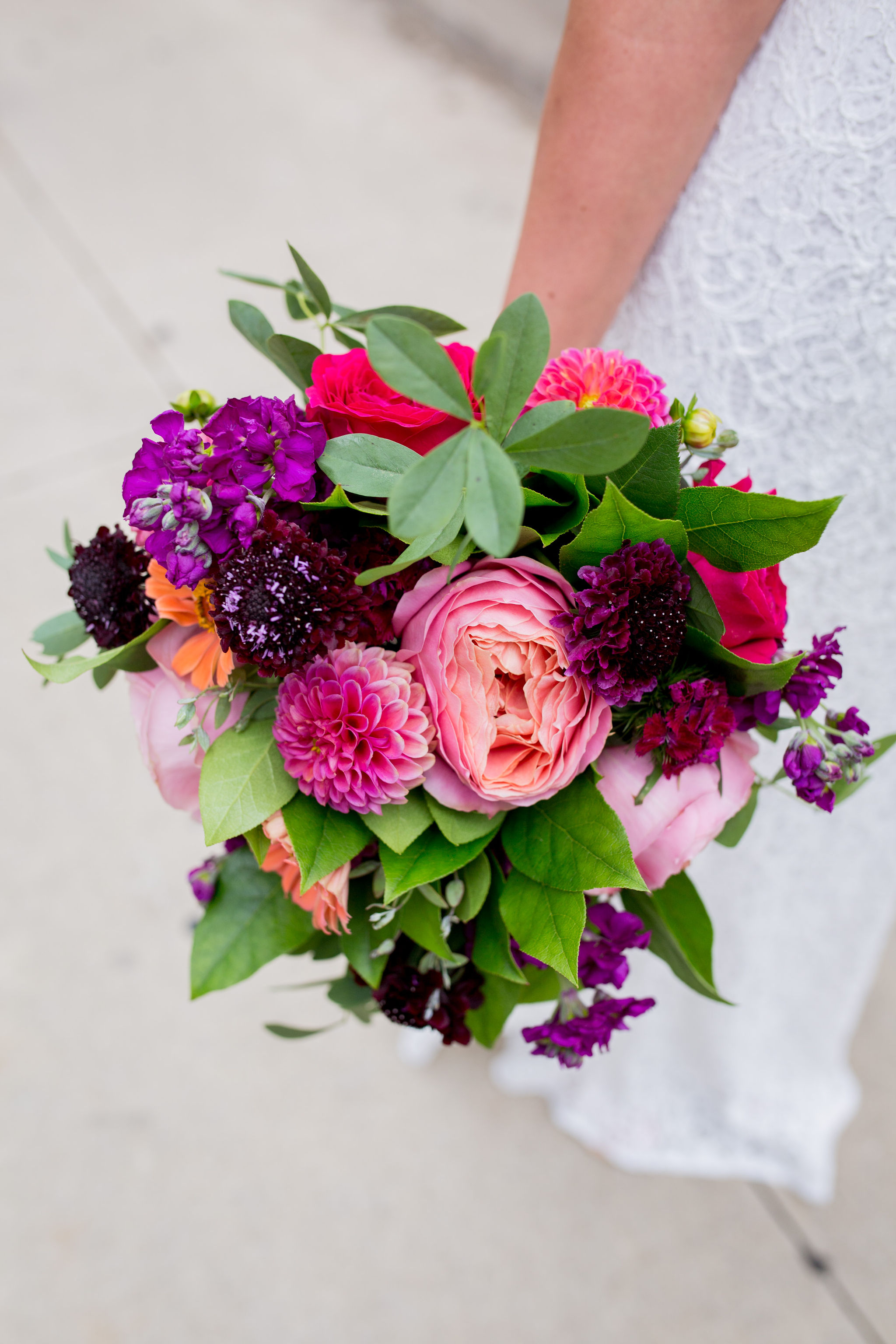 Bright colored bride bouquet with magenta garden roses, dahlias, orange zinnias, purple scabiosa and stock.