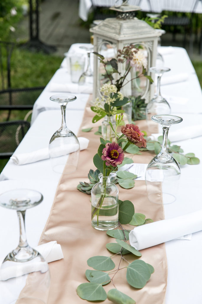 Summer wedding glass bottle arrangements with pink zinnias and eucalyptus.