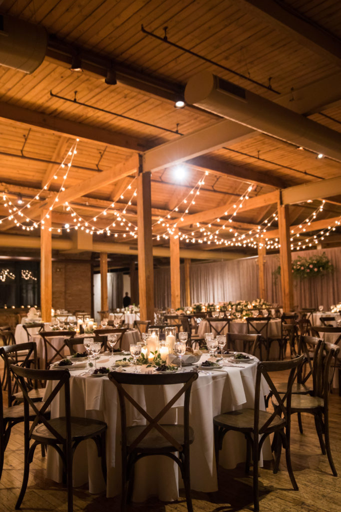 Bridgeport Art Center's Skyline Loft in Chicago wedding reception with rustic tables, cafe lights, foliage and pillar candle centerpieces. 