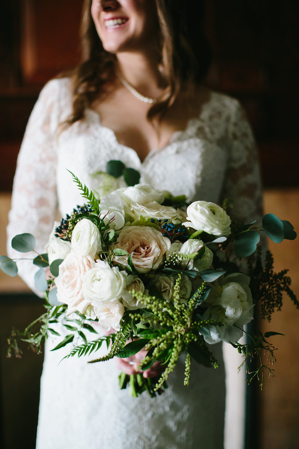 Winter wedding bride with lush bouquet of ranunculus, berries, fern, and blush garden roses.