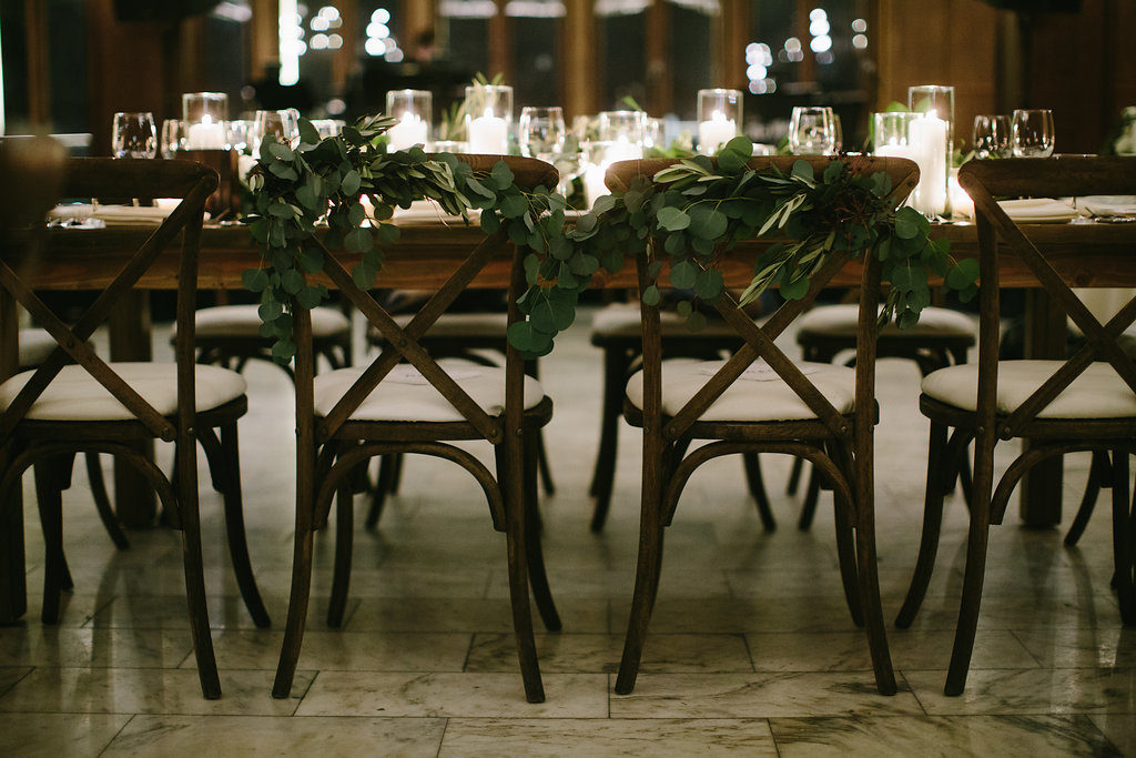 Olive foliage and silver dollar eucalyptus decorated wooden chairs for brides at Chicago Athletic Association winter wedding.