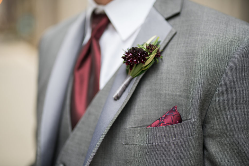 Burgundy scabiosa boutonniere worn on groom with grey suit and ruby tie.