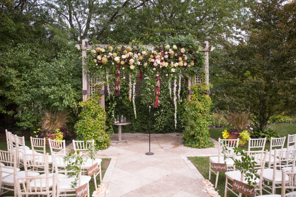 Hanging flower ceremony altar for outdoor fall wedding with garden roses, hydrangea, and burgundy and ivory dahlias.