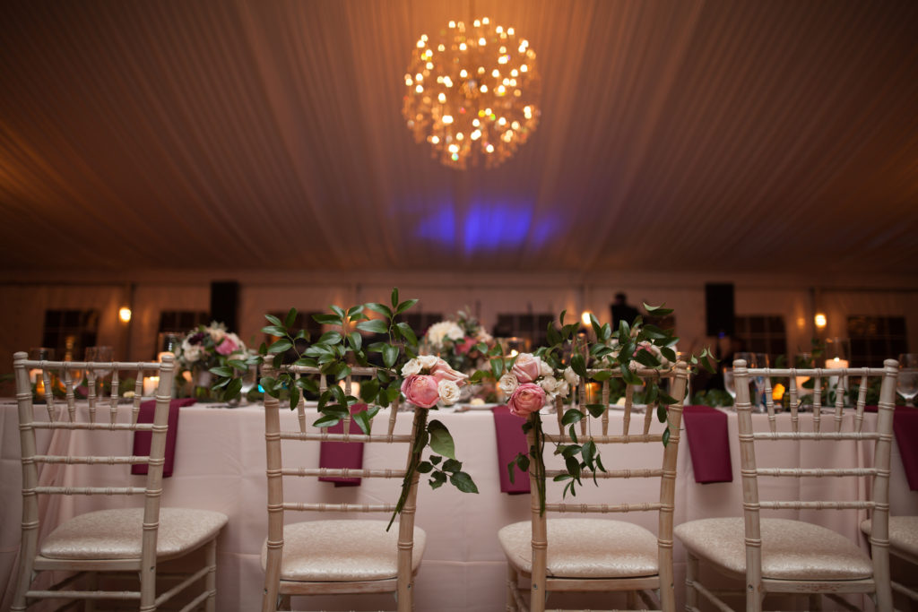 Wedding couple's ivory bamboo chairs with pink and ivory garden roses and greenery for a formal tent reception.