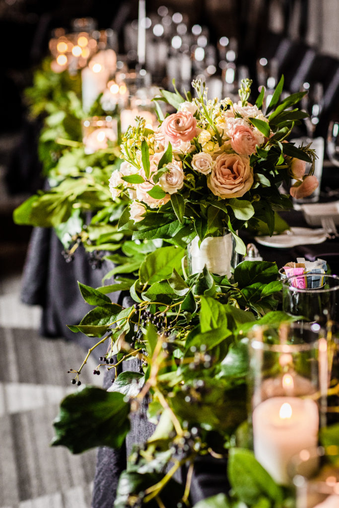 Foliage and berry lined table at spring wedding reception, with bride's bouquet of dusty blush garden roses, ranunculus, and yellow stock. 