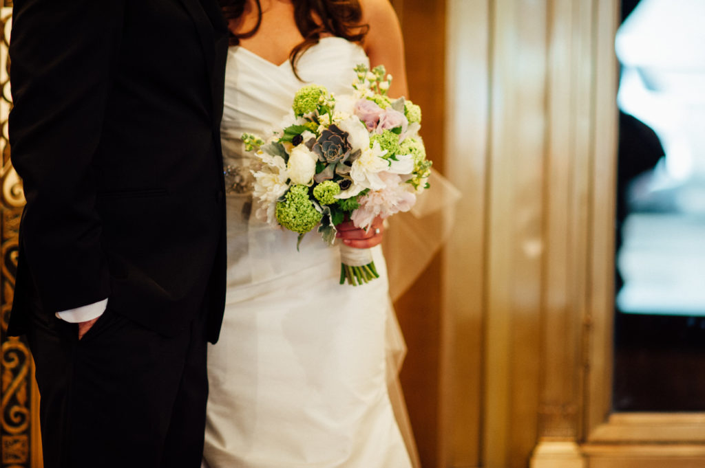 Bride and groom holding bouquet of peonies, succulents, and snowball viburnum for spring wedding celebration.