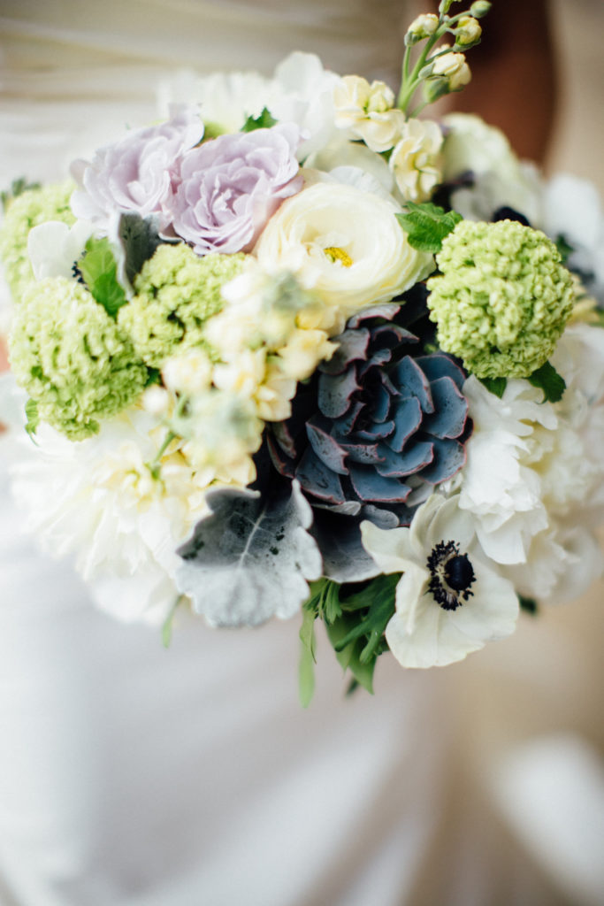Bridal bouquet close-up in pale lilac, ivory, and green, with pale yellow stock, snowball viburnum, succulents, anemone, and peonies.