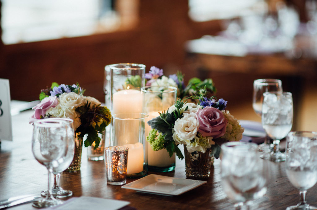 Pillar candles and mercury glass arrangements of garden roses, snowball viburnum, clematis, scabiosa, and hydrangea for spring wedding reception.