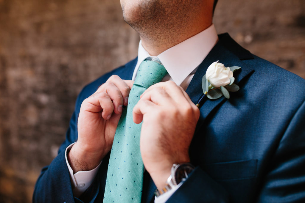 Groom with eucalyptus and white rose boutonniere with navy band and teal polka dot tie for spring wedding at Moonlight Studios. 