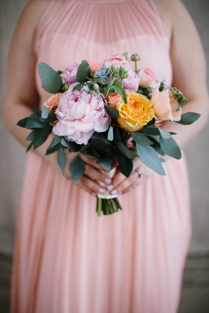 Bridesmaids for spring wedding at Moonlight Studios holding bouquet of pale pink peonies, tweedia, eucalyptus, and garden roses in pale orange and coral.