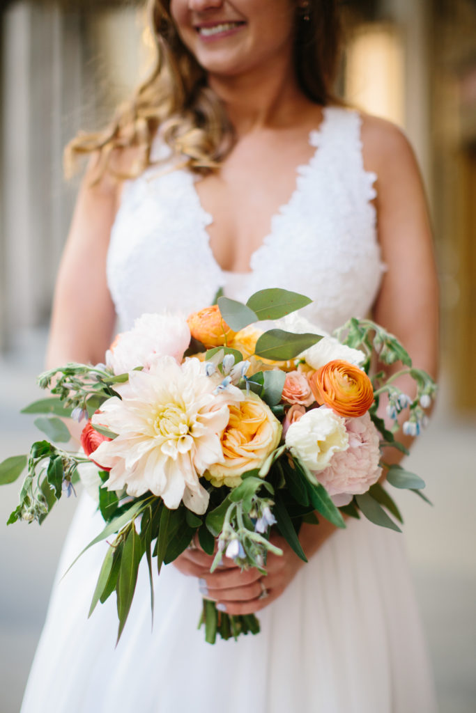 Spring bride with colorful bouquet of dahlias, orange and coral ranunculus, blue tweedia, pink peonies, eucalyptus, and garden roses.