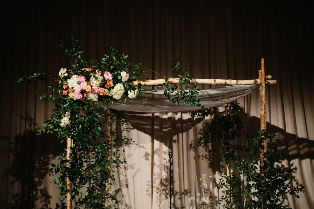 Ceremony altar of birch, draped fabric, foliage and focal flowers of white hydrangea, pink and orange garden roses.