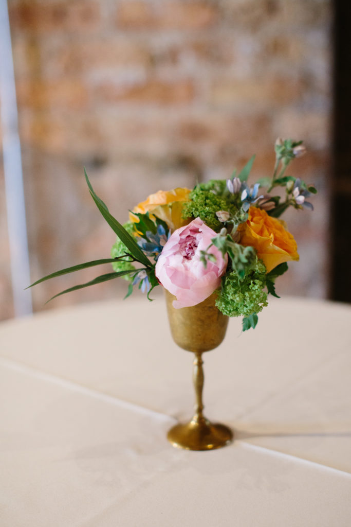 Brass vase highboy arrangement for spring wedding at Moonlight Studios with pink peonies, orange garden roses, snowball viburnum, and blue tweedia.