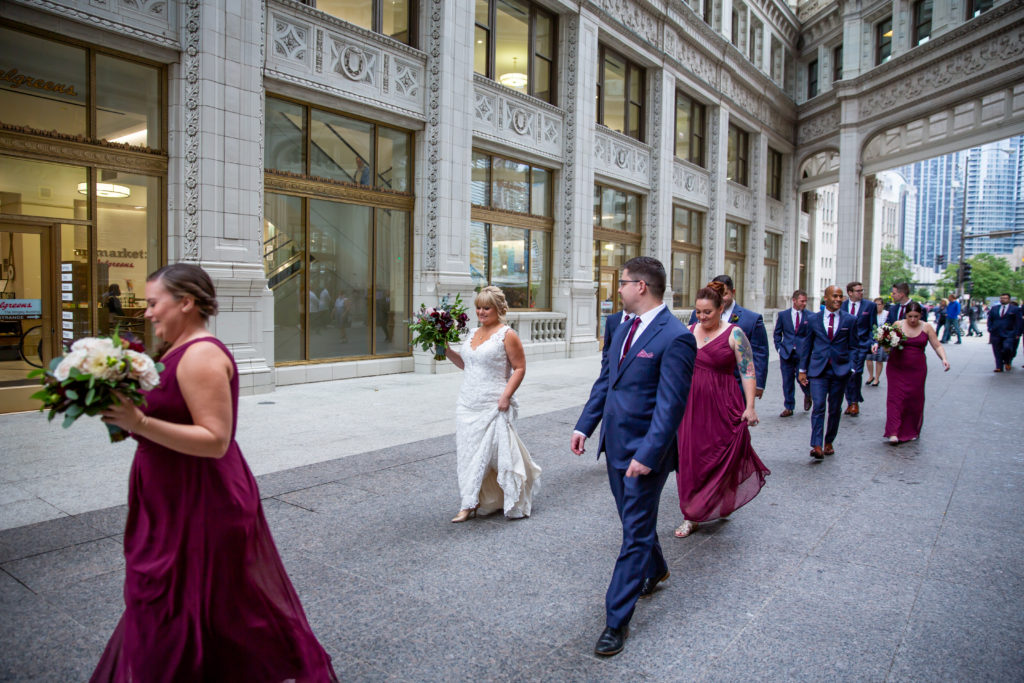 Wedding party in maroon gowns, walking through historic downtown Chicago with bouquets of protea, dahlias, garden roses, scabiosa, purple acacia, and white majolika. 