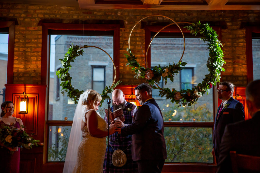 Bride and groom presenting vows before the altar of hanging floral wreaths in Revolution Brewing for a fall wedding. 