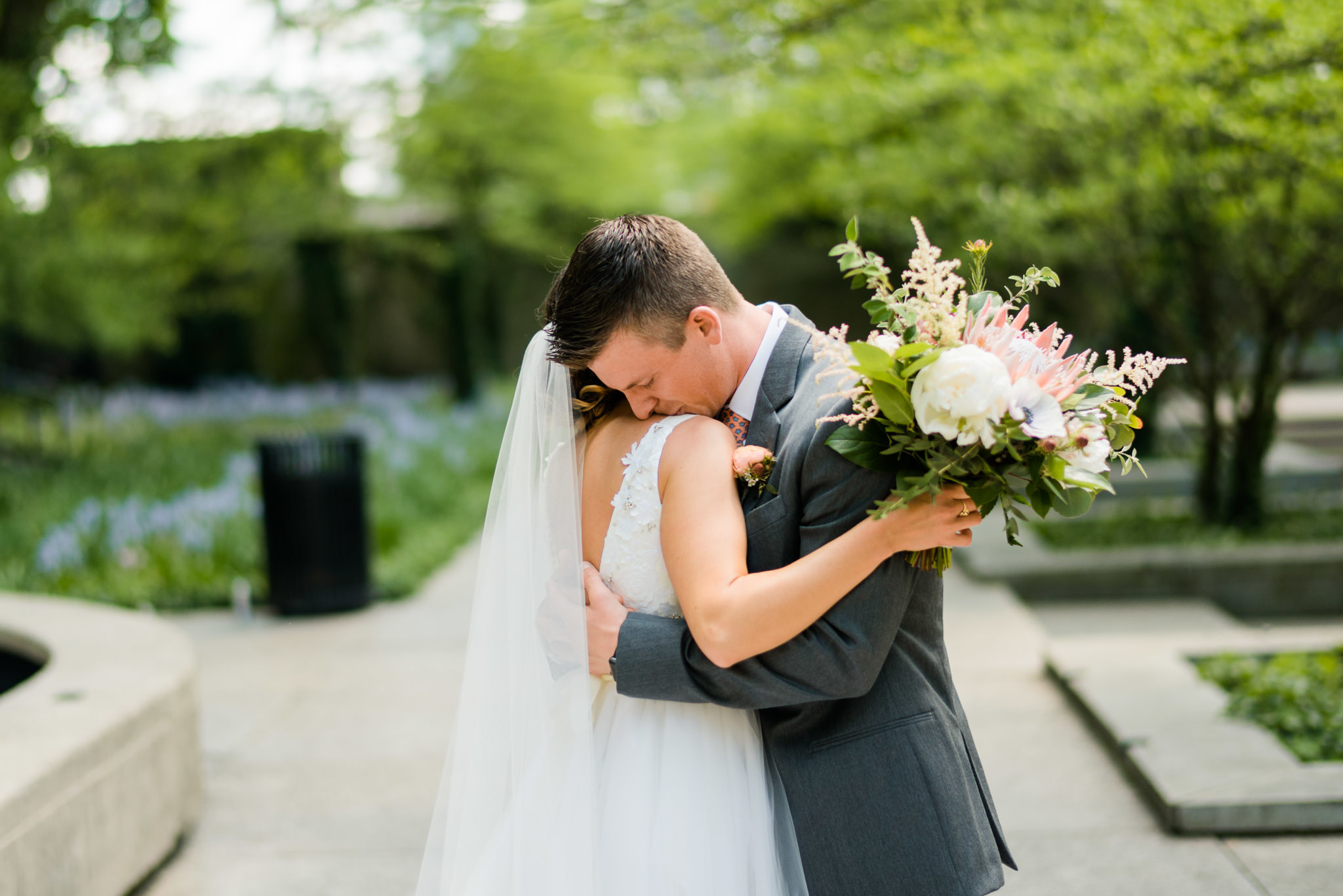 Bride and groom hug in South Garden at the Art Institute of Chicago for spring wedding at River Roast, with bouquet of protea, peonies, and astilbe.