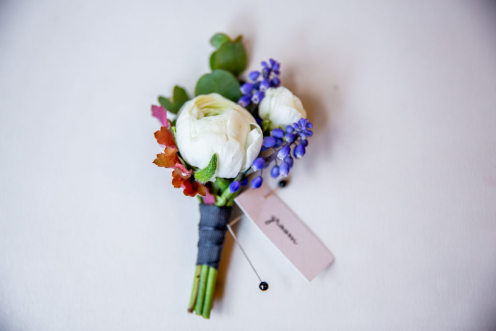 White ranunculus and grape hyacinth boutonniere for a vibrant spring wedding.