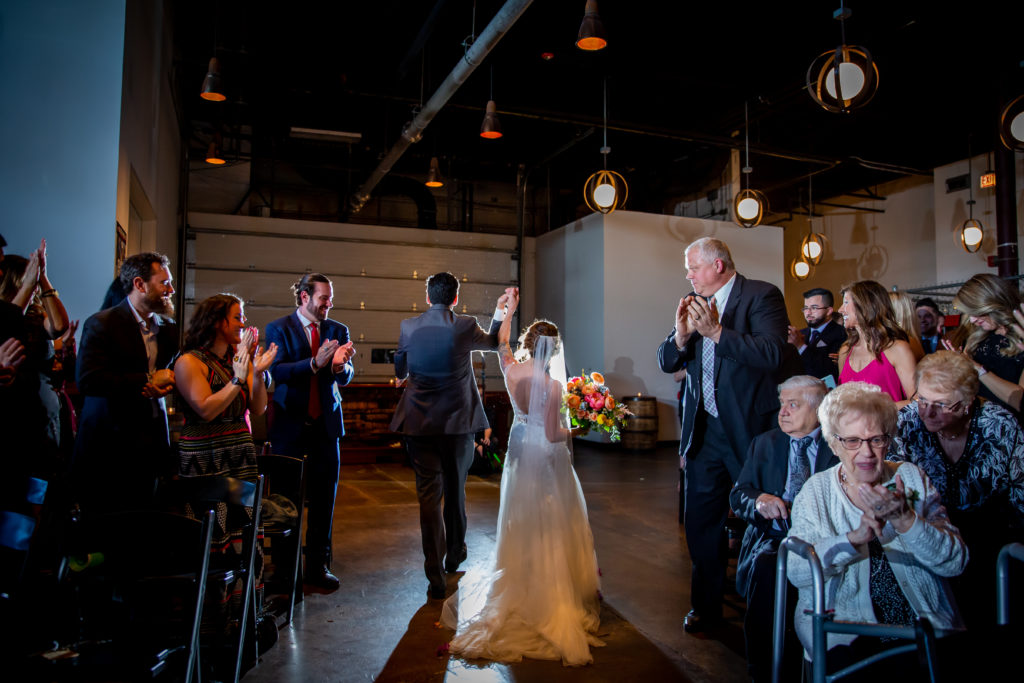 Spring bride and groom ceremony at Revolution Brewing, holding vibrant bridal bouquet of yellow poppies, peach ranunculus, and magenta peonies.