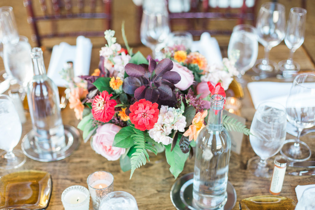 Miniature mercury glass vases with fall wedding reception arrangements of pink garden roses with red zinnias, fern, and blush stock on rustic wooden tables at City View Loft Chicago.