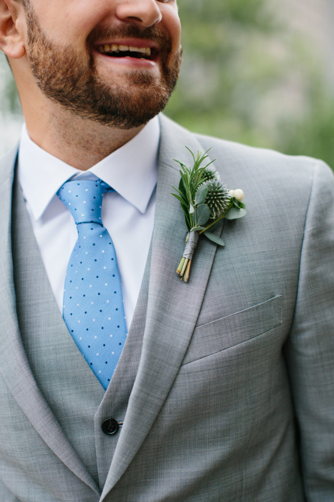 Groom with blue tie and boutonniere of thistle, rosemary, and white hypericum berries for summer wedding at Adler Planetarium.
