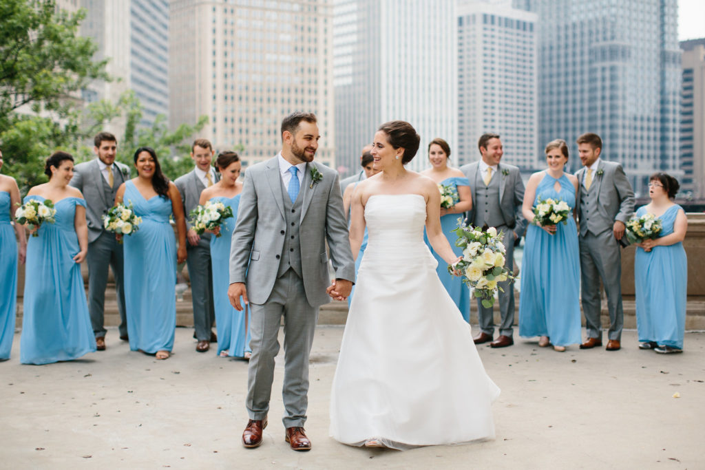 Bride and groom outdoor for celestial summer wedding at Adler Planetarium with blue bridesmaids dresses and bouquets of pale yellow stock, ivory ranunculus and garden roses, succulents, and eucalyptus. 