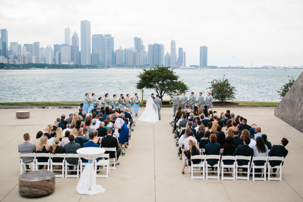 July outdoor summer wedding at Adler Planetarium with chair swags and silver lanterns lining the aisle made from blue hydrangea and ivory garden roses.