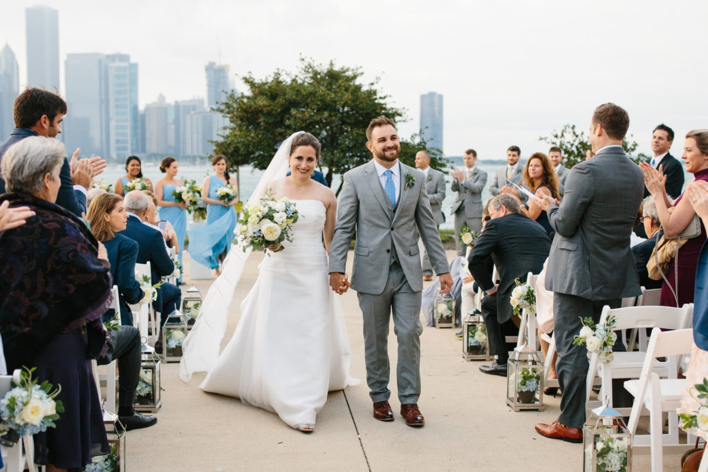 Bride and Groom at July outdoor summer wedding at Adler Planetarium with chair swags and silver lanterns lining the aisle made from blue hydrangea and ivory garden roses.