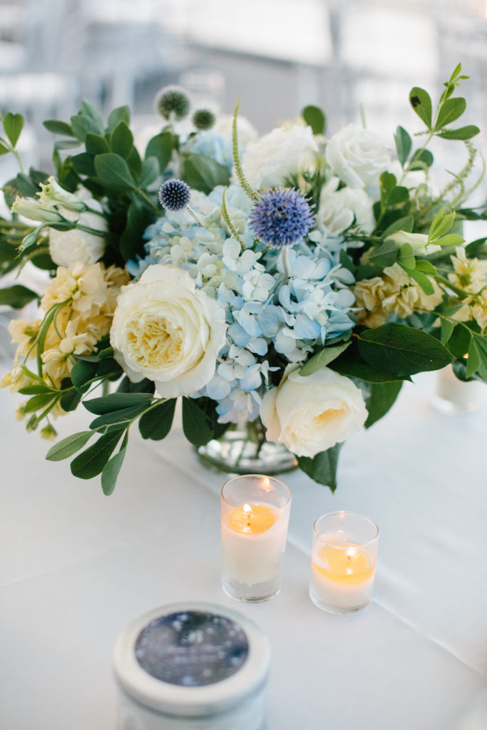 Reception arrangement with blue thistle, hydrangea, pale yellow stock, ivory garden roses and lisianthus at Adler Planetarium for summer wedding. 
