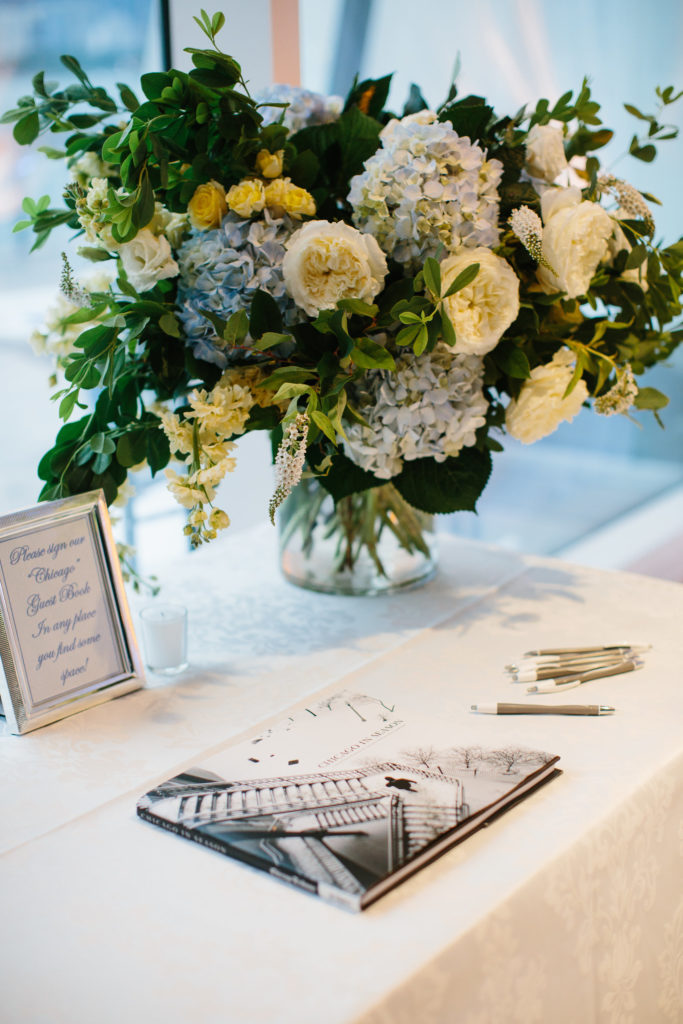 Guest book table with lush bouquet of yellow spray roses, ivory garden roses, veronica, blue hydrangea, and foliage for summer wedding at Adler Planetarium. 
