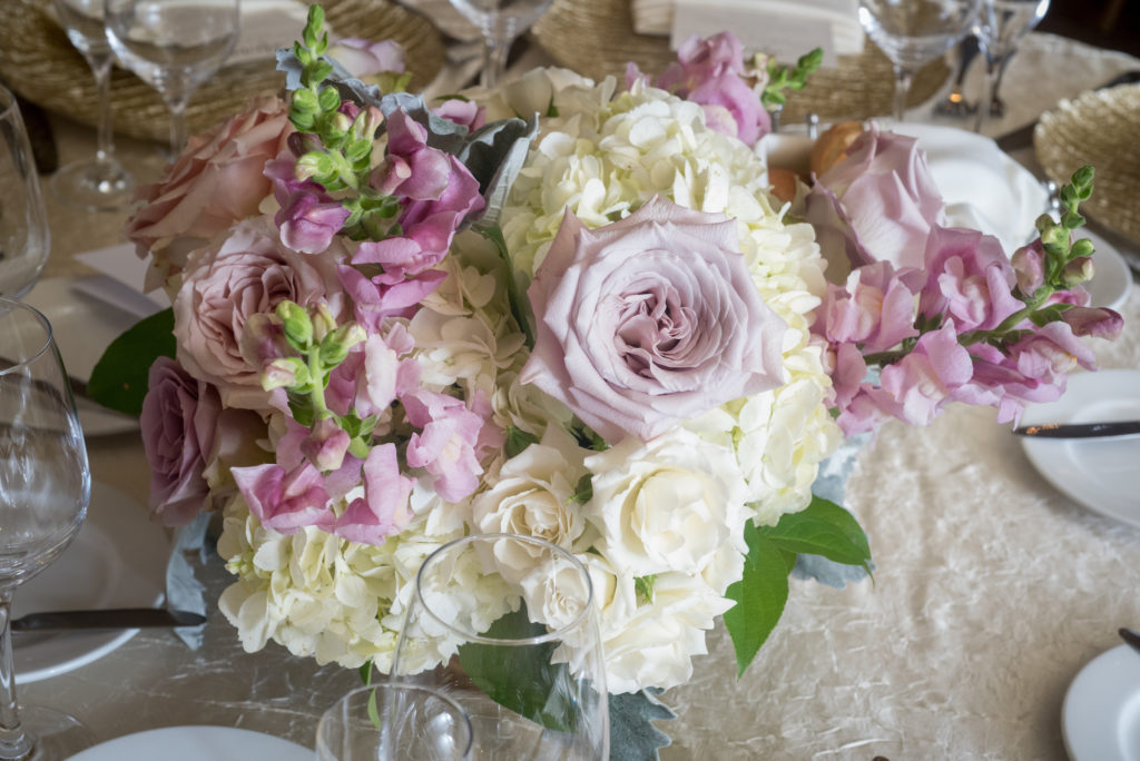 Elegant and feminine spring wedding reception arrangement of lilac stock, ivory hydrangea an spray roses and mauve garden roses.