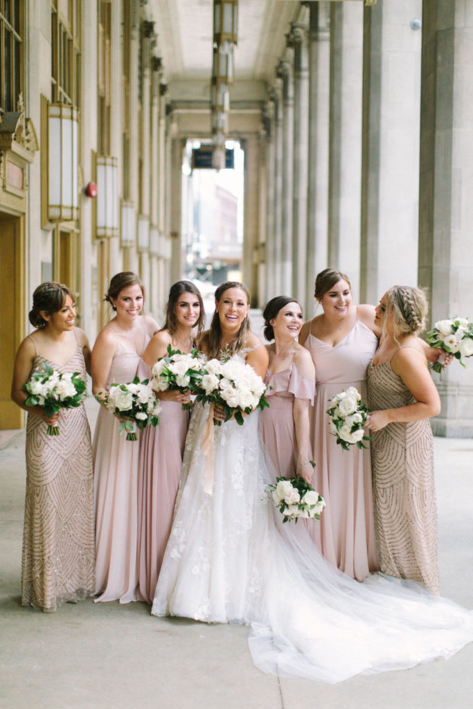 Bride and bridesmaids in blush and dusty rose dresses with ivory bouquets of garden roses, majolica roses, peonies, and ranunculus for an outdoor summer wedding.