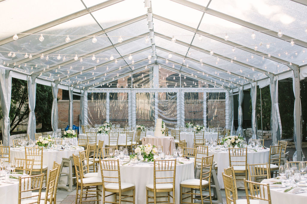 Romantic tented outdoor wedding reception at Chicago Illuminating Company with brushed gold Chiavari chairs, pale linens, globe string lights, and garden inspired bouquets of ivory garden roses, pale pink peonies, and flowering branches.