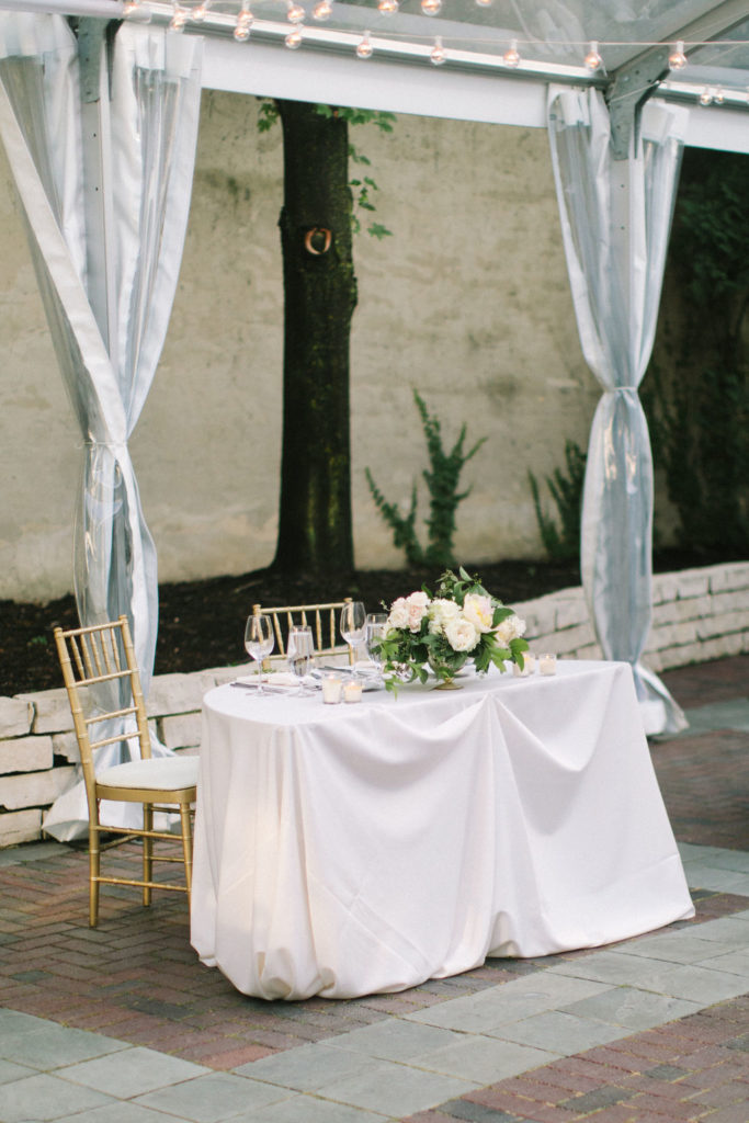 Romantic outdoor tented summer wedding reception in Chicago with a classic and romantic sweetheart table with a pale arrangement of blush peonies, ivory garden roses, and hydrangea.