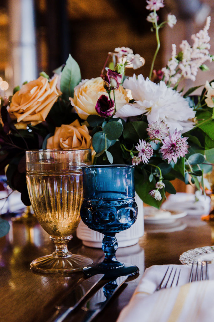 Reception table details with colorful flowers of lisianthus, peonies, astilbe, and garden roses at this couple’s Salvage One wedding in Chicago, plus vintage china and votives. 
