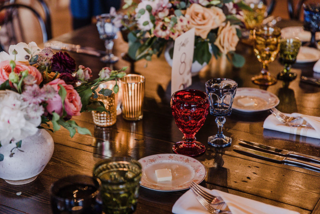Reception table details with colorful flowers of lisianthus, peonies, astilbe, and garden roses at this couple’s Salvage One wedding in Chicago, plus vintage china and votives. 