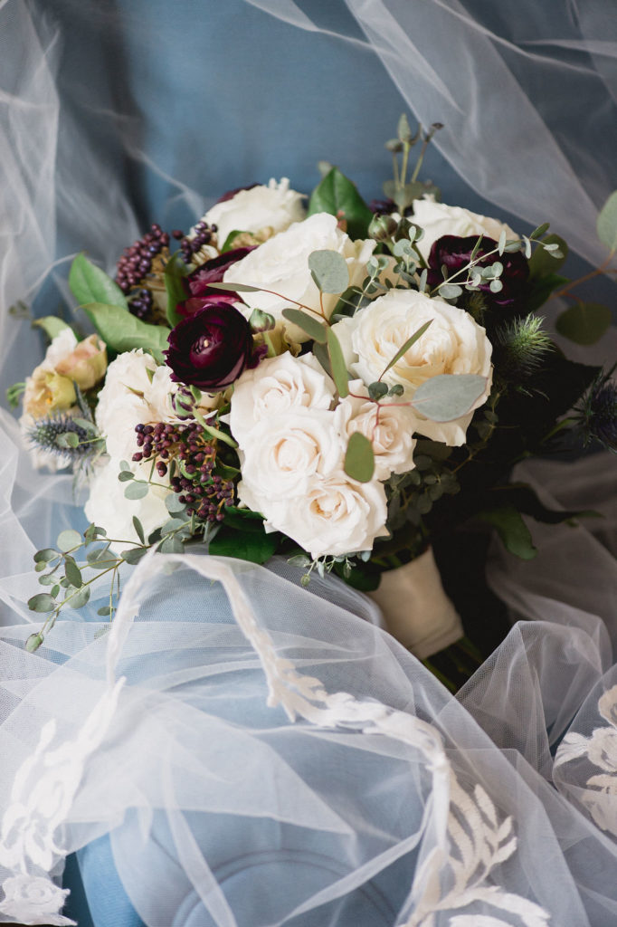 Bridal bouquet detail for fall wedding with plum ranunculus, berries, ivory spray roses, thistle, eucalyptus.