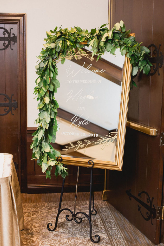 Foliage draped over golden etched mirror for fall wedding signage. 