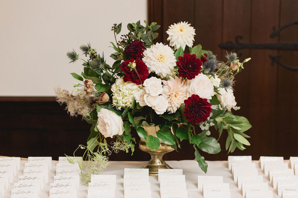Escort table arrangement for a traditional fall wedding with flowers like burgundy and blush dahlias, ivory garden roses, thistle, lisianthus, and hydrangea.