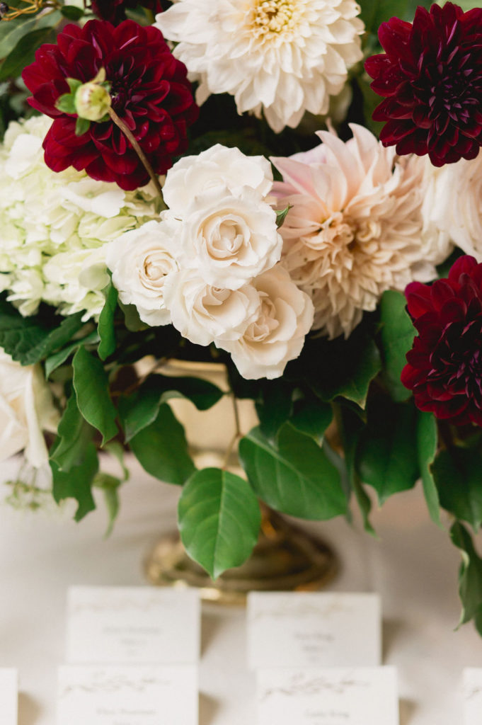 Fall wedding arrangement detail at escort table with blush spray roses, full burgundy and blush dahlias, and pale green hydrangea.