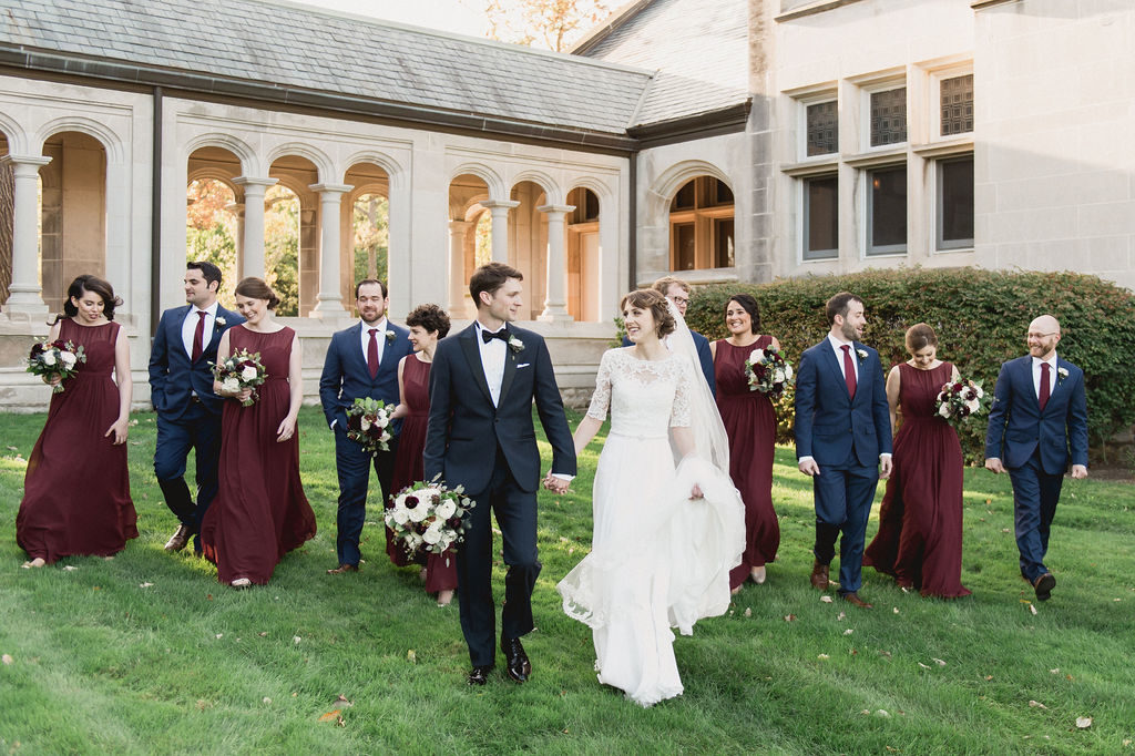 Bride and groom at their traditional fall wedding, with bouquets of burgundy and ivory dahlias, plum ranunculus, garden roses, thistle, berries, lisianthus, and dusty green foliage. 