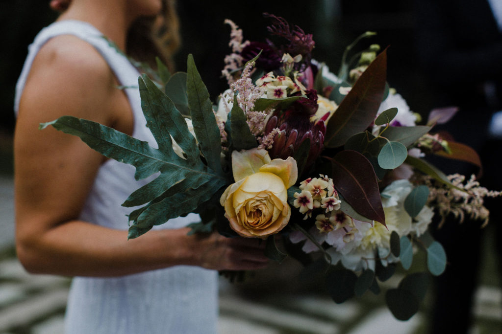 A dramatic bouquet for a Chicago wedding at Salvage One, with a colorful bohemian style and flowers like protea, astilbe, garden roses, and peonies.