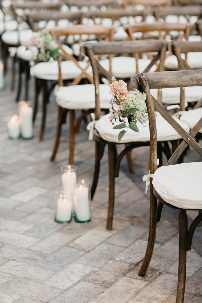 Outdoor late summer wedding ceremony at Bridgeport Art Center Sculpture Garden with hanging aisle decorations of pale pink stock, ivory spray roses, pale green hydrangea, and daisies -- elegant pillar candles lined the aisle. 