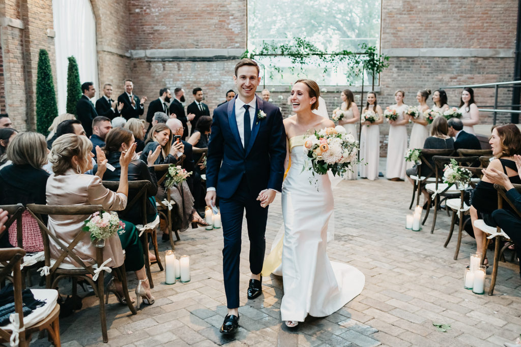 An elegant late summer wedding ceremony reception in Bridgeport Art Center's Sculpture Garden, featuring an industrial altar with a hanging flower installation of ranunculus and stock. 
