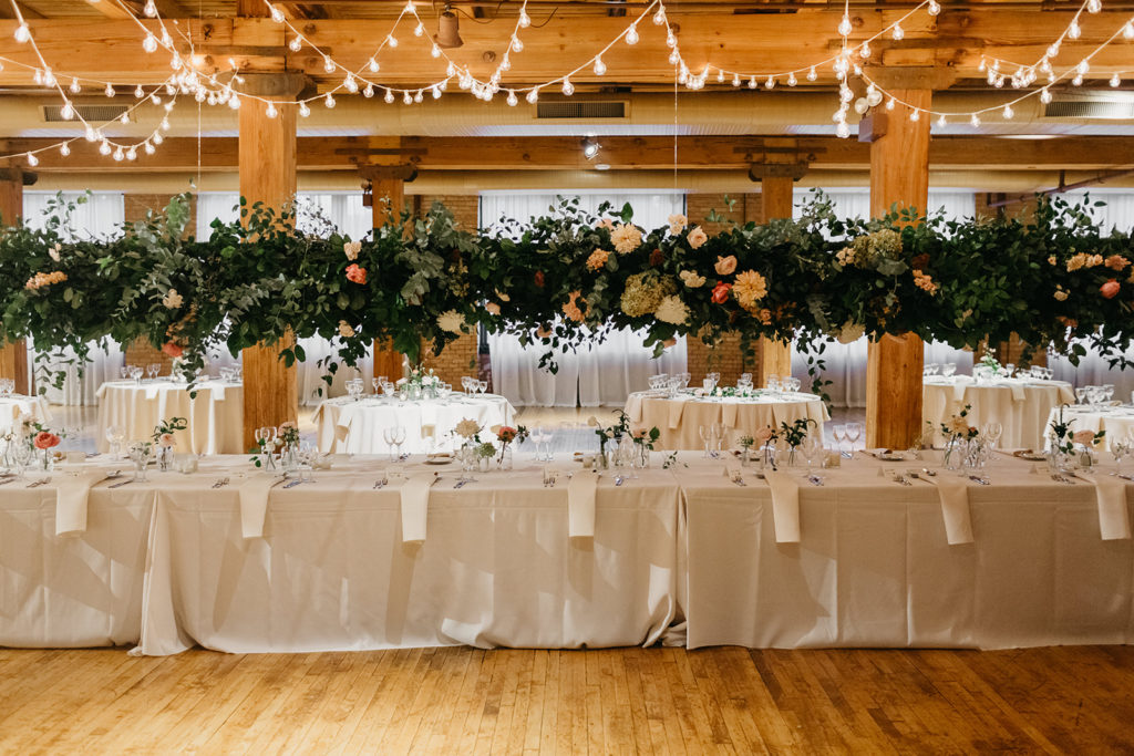 Bridgeport Art Center's Skyline Loft in Chicago wedding reception with hanging floral installation and cafe lights over head table with blush dahlias and pink garden roses.