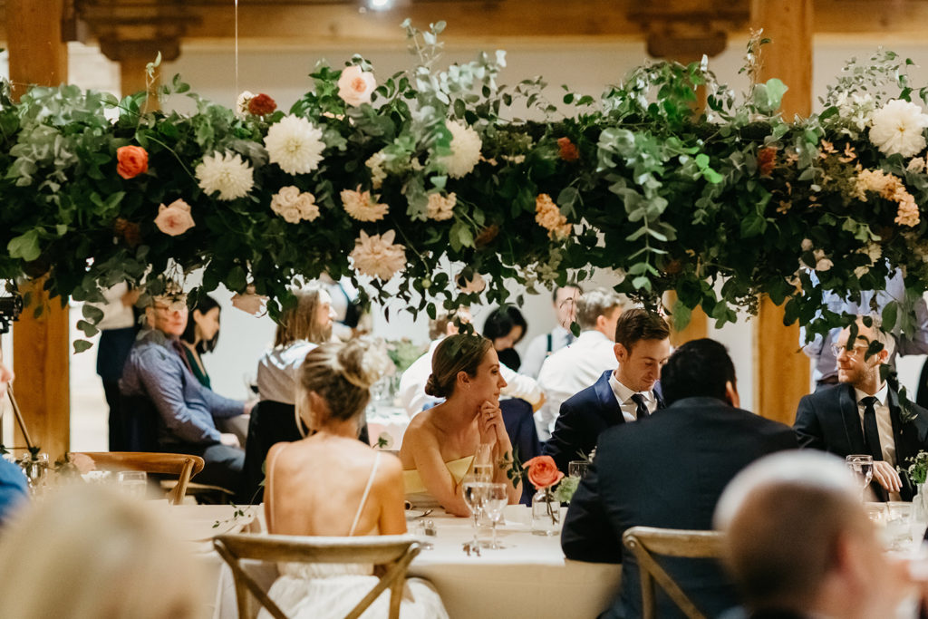 Hanging cafe lights and a hanging floral installation above an elegant long center table for a late summer wedding reception at Bridgeport Art Center's Sculpture Garden.