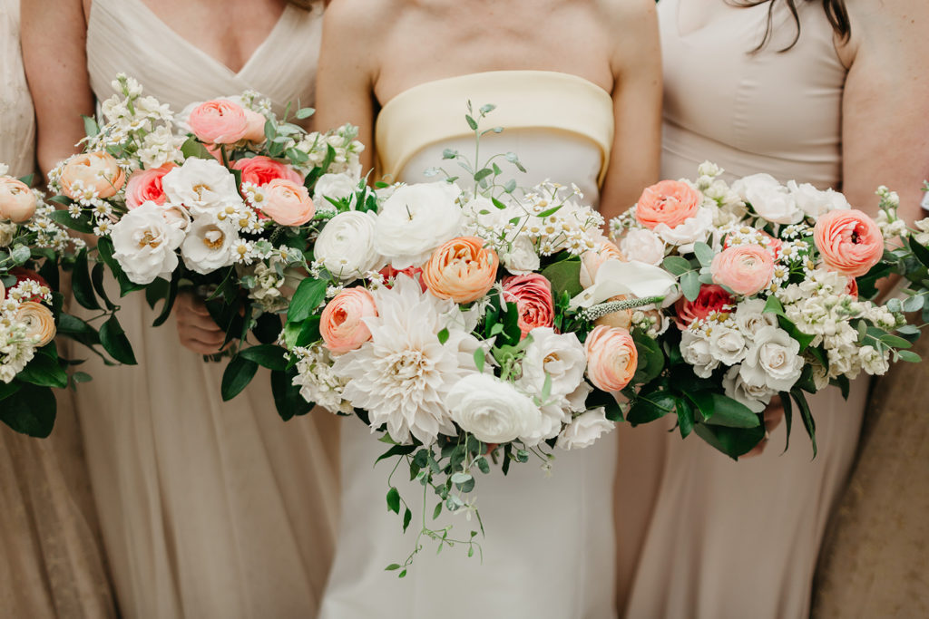 Bride and bridesmaid bouquets with bright pink garden roses and ranunculus, peach ranunculus, and white dahlias, roses, ranunculus, and daisies.