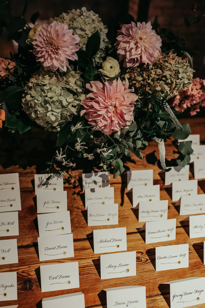 Escort card table for a late summer wedding at Bridgeport Art Center, featuring a lush arrangement of pink dahlias, clematis, pale green hydrangea, white veronica, and ranunculus. 